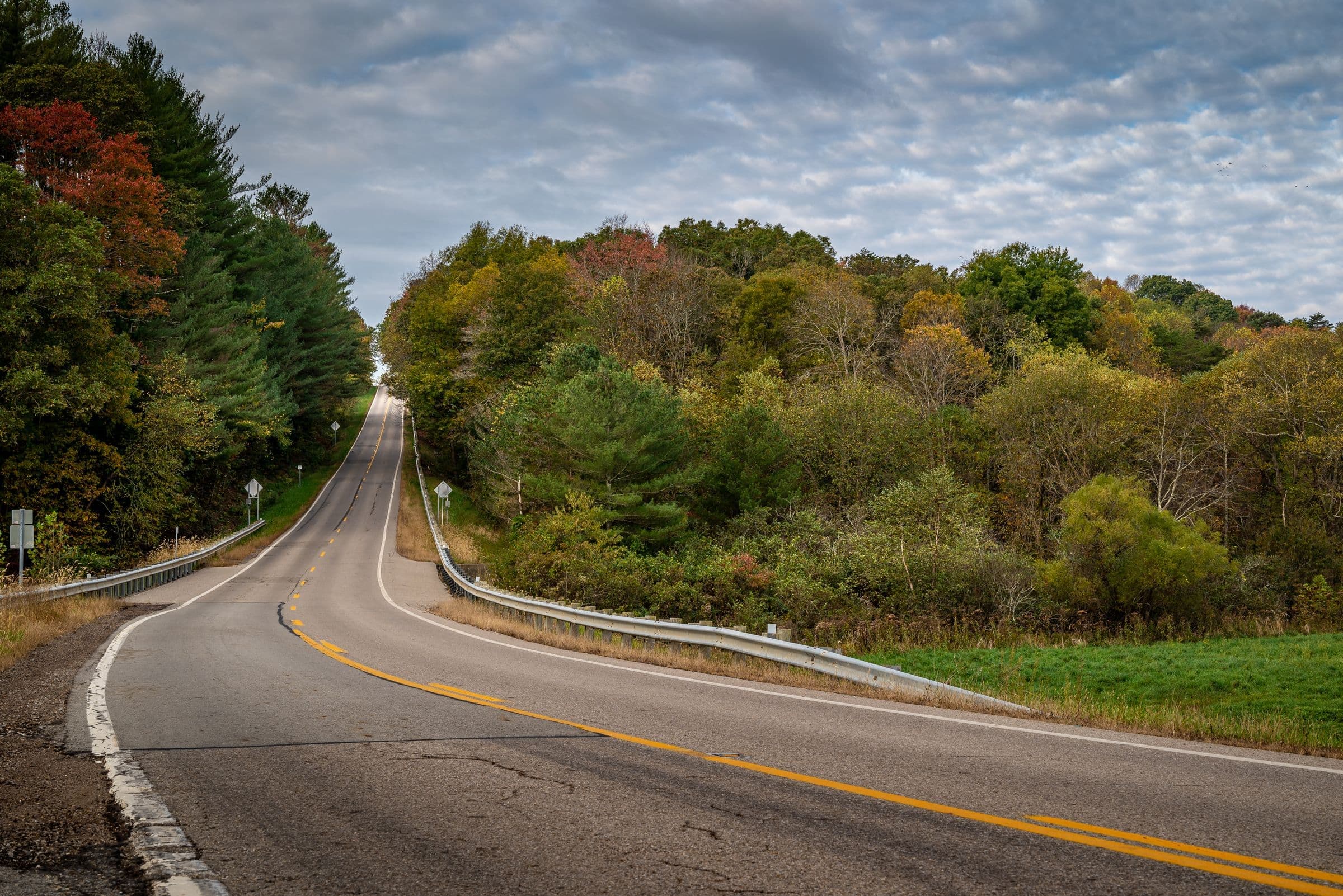 A two-lane road curving through a wooded river valley in autumn near Dell Rapids, where we do mobile windshield replacement
