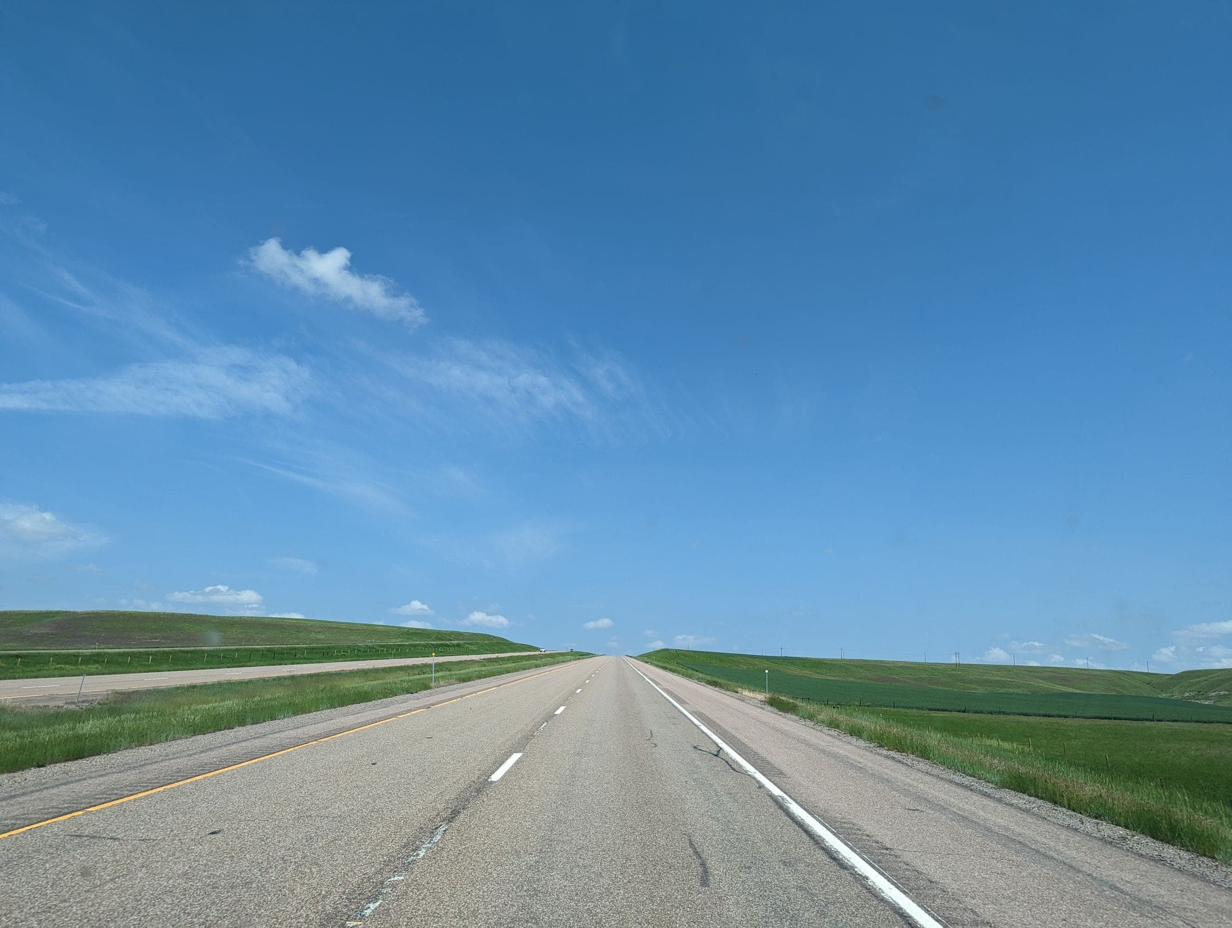 A wide, flat four-lane highway between green fields near Tea, where we do mobile windshield replacement